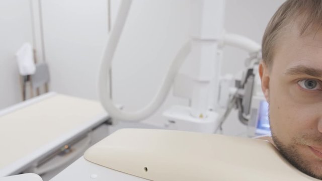 Tired male patient at lungs rontgen examining procedure waiting the starting close up. Doctor preparation radiology medicine equipment for x-ray photo in modern technology clinic at background