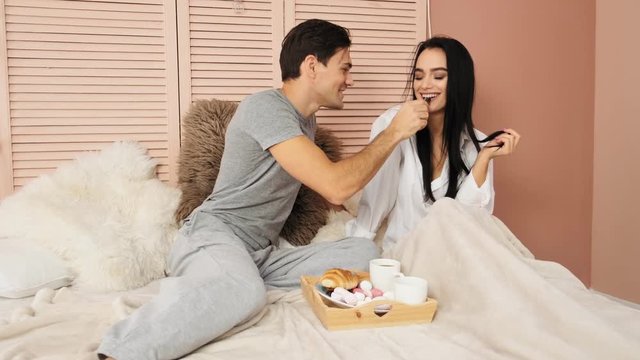 Loving couple having breakfast in the bed of the hotel and feeding each other. Slow motion