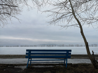 Fototapeta na wymiar Blue bench on the background of the empty Russian winter landscape in the beginning of spring