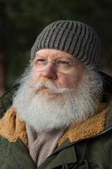 Stylish senior caucasian man in knitted cap and eyeglasses against dark natural winter background. Close up face of elderly hipster with splendid mustache and beard.