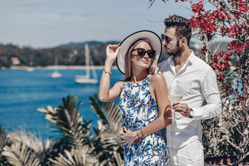 young fashion couple in sunglasses standing and posing at the camera on sunny summer day.Trip to warm destination. Honeymoon.Beautiful sea and floral landscape. Phuket. Thailand.