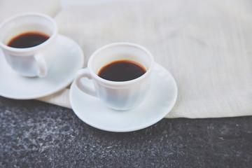 Two white cups of espresso on grey grunge background.