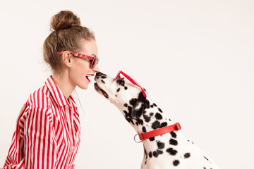 Portrait of happy young woman in red glasses sitting with her dalmatian dog, that licking her face....