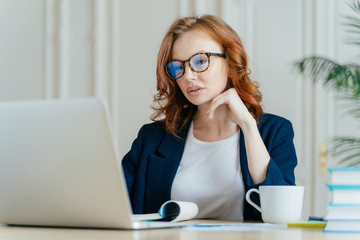 Shot of atttactive businesswoman concentrated in monitor of laptop computer, has serious focused...