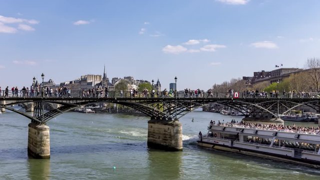 Timelapse: People walking on Pont des Arts bridge on the Seine river with tourists boat traffic and Ile de la Cite in background - Paris, France