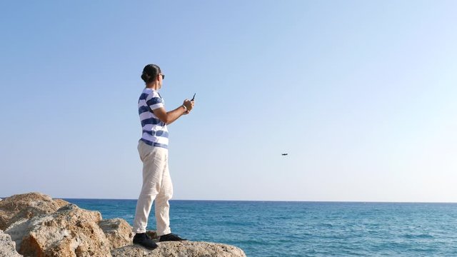 Young adult man using small drone on beach, send it flying to sea and back