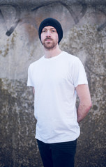A portrait of young handsome man with stubble and a beanie hat standing alone and contemplating life by the quiet sea, surrounded by raw concrete sea defence wall.