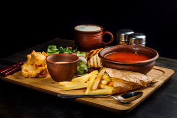 Lunch on a wooden board. Soup, chicken breast, salad and sauce.