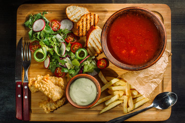 Lunch on a wooden board. Soup, chicken breast, salad and sauce.