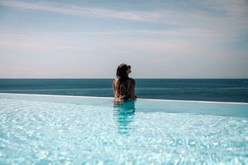 Young woman relaxaing in the swimming pool looking at the ocean view in background l. Beautiful...
