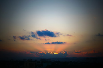 Fototapeta premium light rays of sun in sunset sky above the city