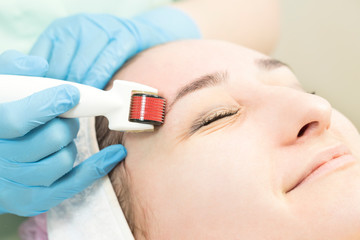 The woman undergoes the procedure of medical micro needle therapy with a modern medical instrument derma roller.