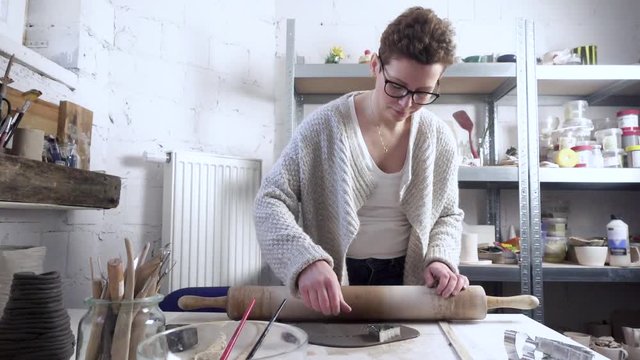 Woman making clay decorations, cutting out shapes.