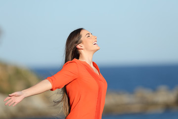 Happy woman in orange breathing fresh air in the coast