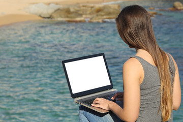 Woman using laptop showing blank screen on the beach