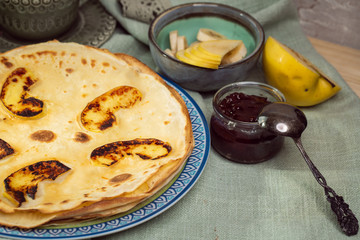 Cooked crepes folded on a plate with jam and apples