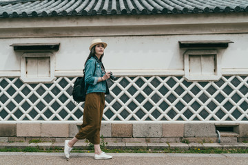 Fototapeta na wymiar full length tourist walking along small stone street beside huge stone wall in osaka castle town. young asian woman travel photographer holding professional camera sightseeing quiet old place japan