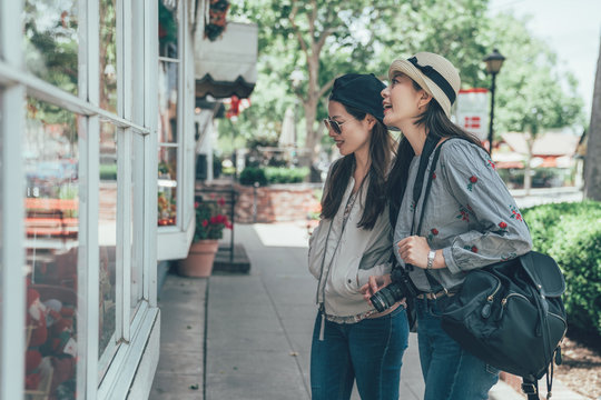 group of asian women tourist standing outside store looking window talking smiling. female travel backpacker with camera in solvang santa barbara denmark town in usa. young girls cheerful shopping.