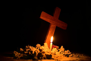 Burning candle under Jesus cross in a cemetery against black background. 