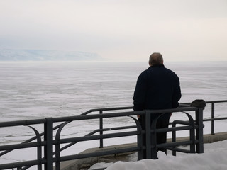 An elderly man looks into the distance on the waterfront against the winter landscape