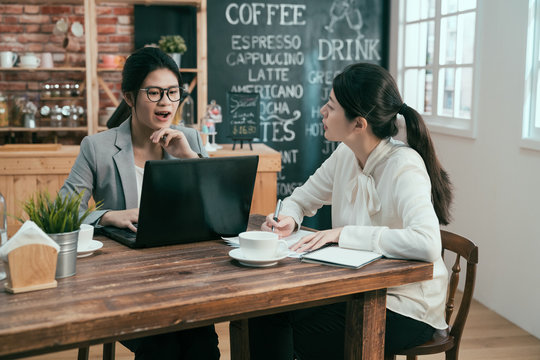 Active Young Smart Confident Businesswoman Helping New Female Worker. Business Freelancer Co Working Space In Cafe Bar Drinking Coffee. Two Asian Office Manager And Employee With Laptop And Notebook