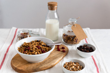 Morning granola breakfast with raisins, cranberries and hazelnuts served with almond milk on a white linen table cloth. Side view