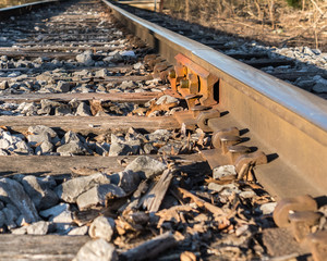 A view down railroad tracks at ground level, focusing on the connection, nuts and bolts that hold the track together. Concepts of strength, connections, and joining