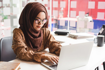 Young asian muslim business woman in smart casual wear working with laptop computer while sitting...