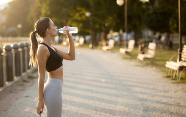Sportswoman making break in jogging, drinking water on quay