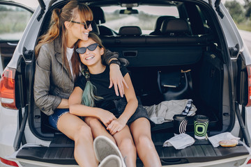 Fashionable mother with daughter. Family is sitting in the trunk. Girl in a black t-shirt