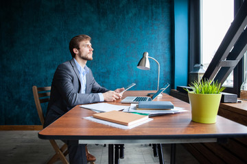Fototapeta premium Shot of young man sitting at table looking away and thinking. Thoughtful businessman sitting in office.