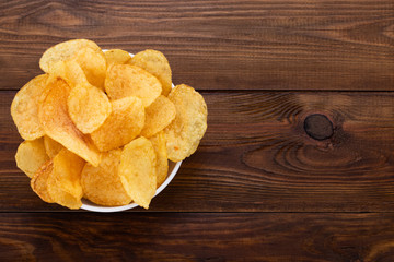 Crispy potato chips in bowl on wooden background. Top view with copyspace