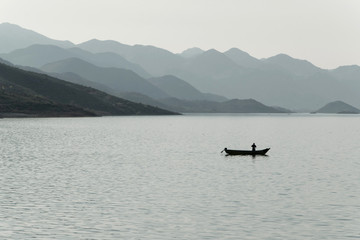 Obraz premium Sylwetka rybaka w małej łodzi w jeziorze, Albania