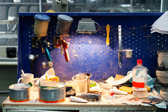 Two body paint gun sprayer red and blue installed on a workbench in a vehicle repair workshop next to another tool and  lighting lamp. Industry in auto service