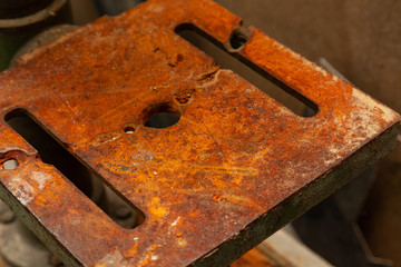 An iron plate with holes covered with a thick layer of rust that eats away metal