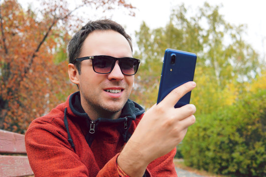 Hipster Man Using Mobile Phone In Autumn Park, Send A Fun Message. Student Chatting With His Collegues From University. Male Student Chatting With Friends