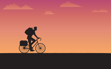 Silhouette cyclist traveler with backpack riding a bike on sunset background