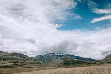Desert green steppe of Mongolia, mountains covered with snow, blue sky and white clouds