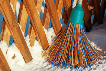 A plastic broom with multicolored bristles of the pile stands in the snow. The concept of cleaning ...