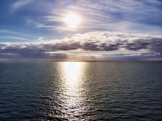 Aerial view above ocean, with  cloudy pastel colored scenic sky and  sun rays hits the water in a hot summer day