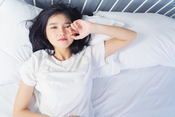 Woman stretching in bed after waking up, back view. Woman sitting near the big white window while stretching on bed after waking up with sunrise at morning, back view.