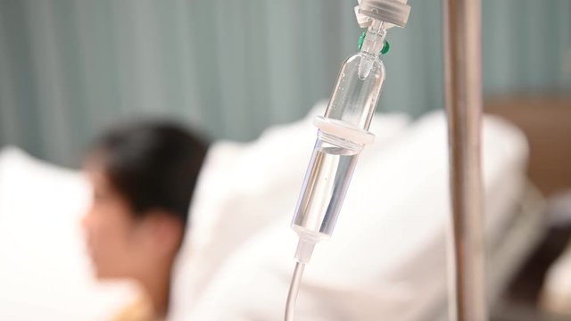 4K Infusion bottle with saline solution for patient in hospital room. Patient on the bed with saline drip. IV fluid use for intravenous volume. Drop of saline solution to help patient.
