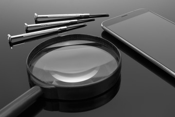 Repair smartphone. Smartphone, screwdriver and magnifier on a dark mirror surface.