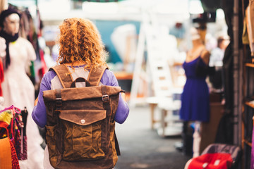 Blonde curly hair woman backpacker traveler viewed from rear at used market enjoying the shopping...