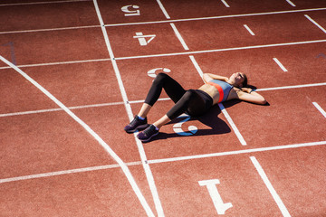 From above view of exhausted teen athlete in sportswear resting on track after finishing tough race