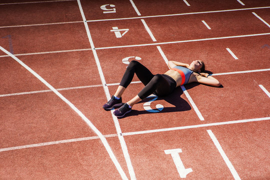 From Above View Of Exhausted Teen Athlete In Sportswear Resting On Track After Finishing Tough Race