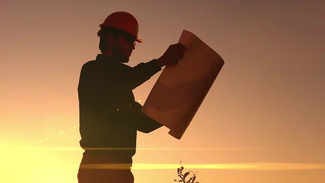 agoma di un giovane ingegnere che osserva la costruzione edile nel cantiere al tramonto. Ripresa al rallentatore.