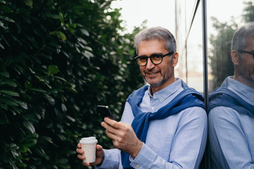 Fototapeta premium businessman outdoor beside glass building using cellphone and drinking coffee