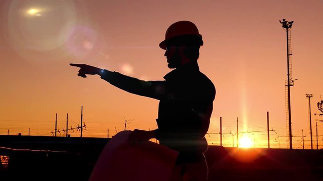 Sagoma di un giovane ingegnere civile edile che indica le operazioni da svolgere a lavoro con il progetto in mano e il caschetto in testa.