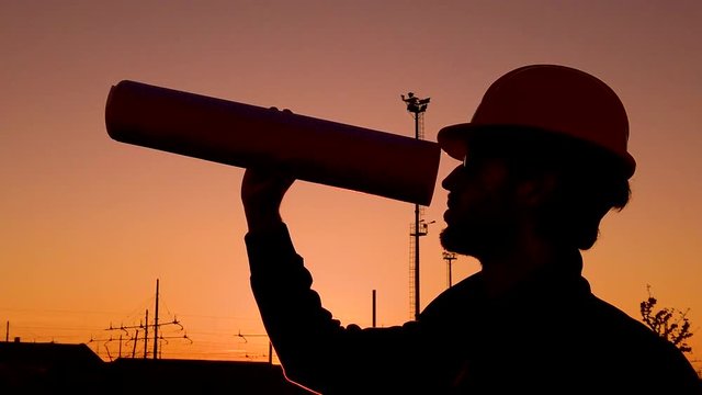 Sagoma di un ingegnere che guarda con il progetto a cannocchiale al tramonto.